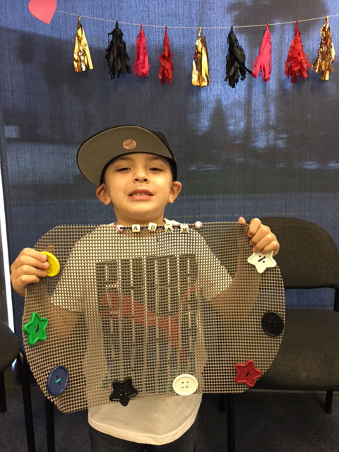 A child is holding up his placemat with shapes attached to it